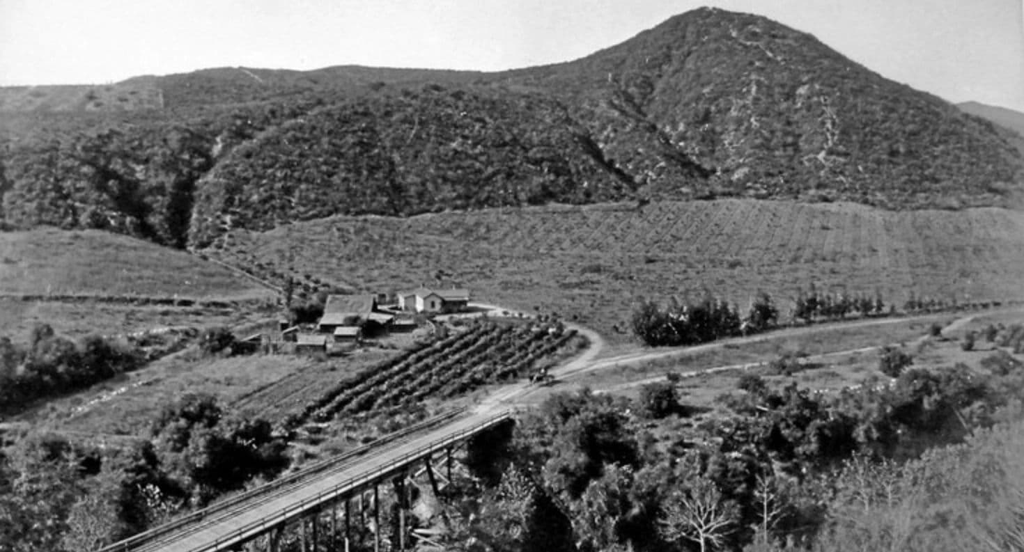 Black and white photo of a rural farm with mountains in the background.